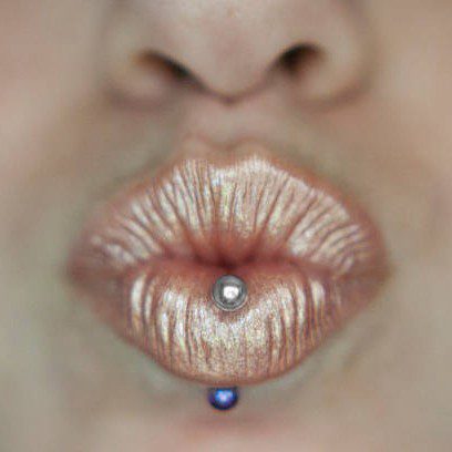 A vertical labret piercing on a woman wearing gold lipstick.